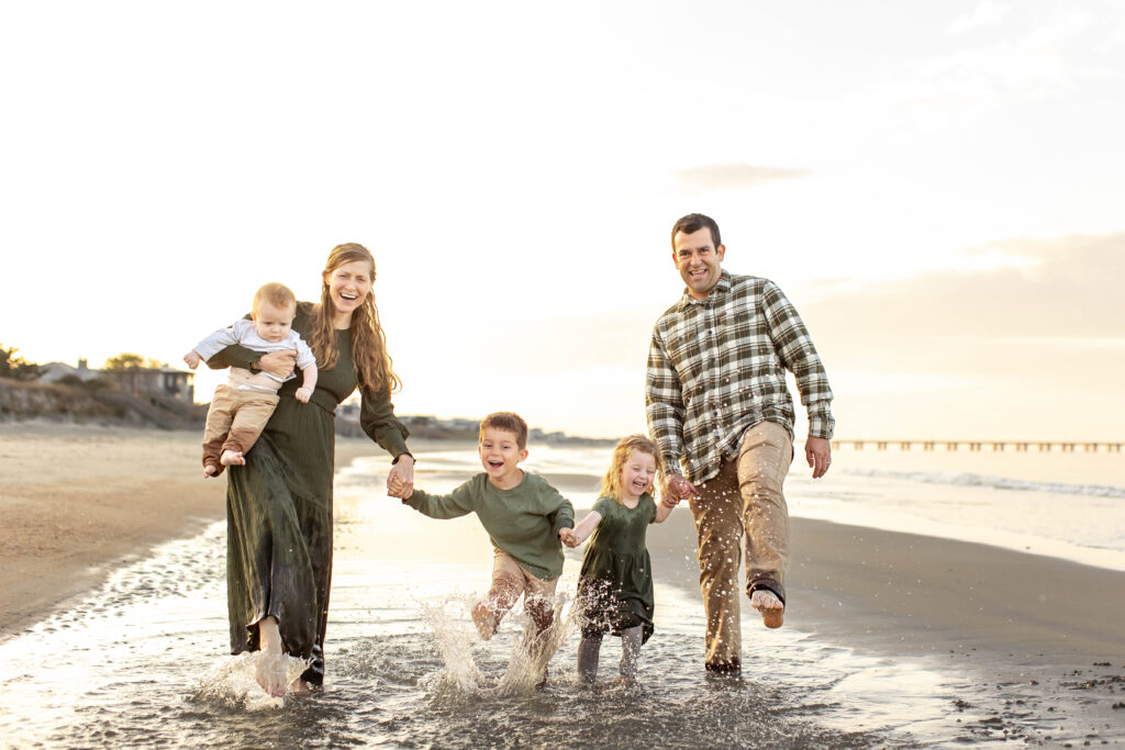 A beautiful young family of five plays together, kicking and splashing water laughing joyfully as the golden sun sets behind them on the bay in Virginia Beach, Virginia.